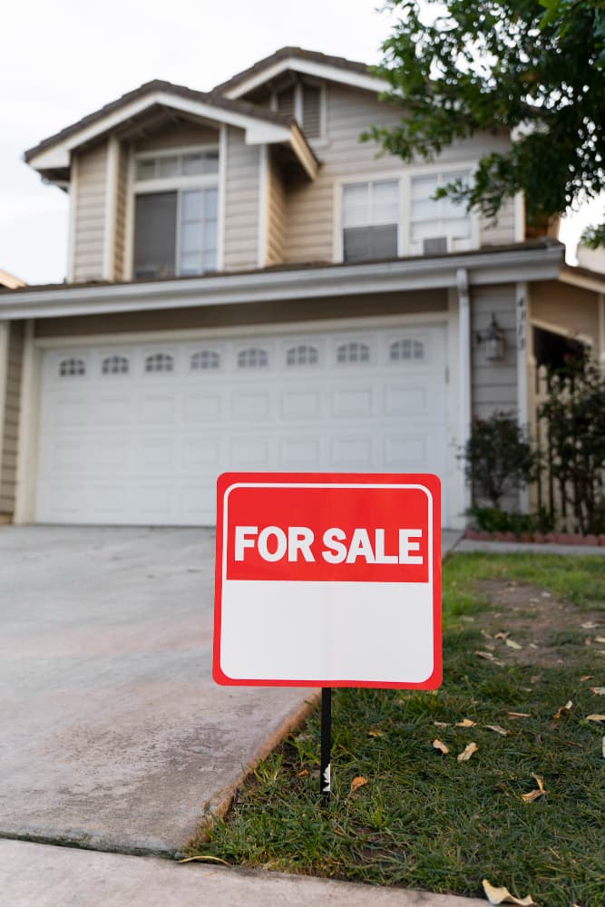 The exterior of a listed house with a For Sale sign in the yard